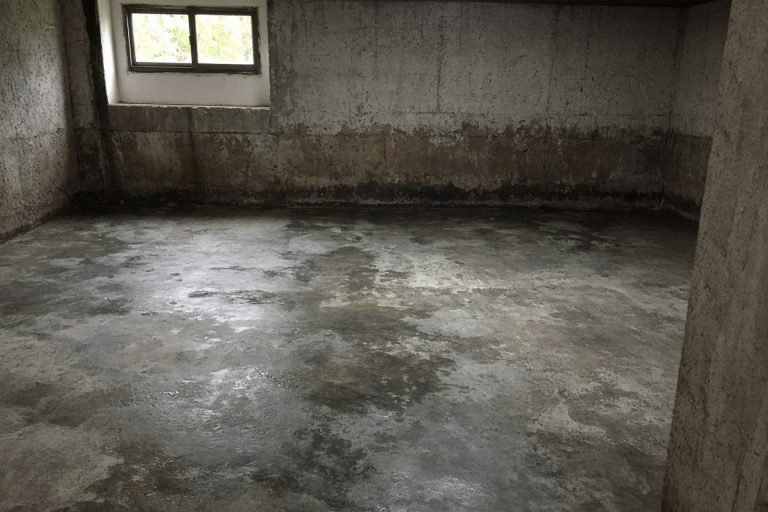 Damp basement floor with dark stains along the wall — Basements in Burns Harbor