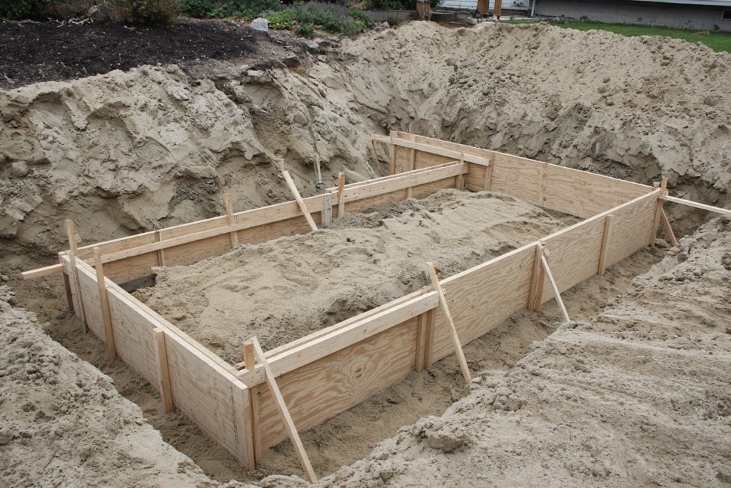 Wood forms set in a sandy basement hole on a slope — Concrete Basements in Ogden Dunes
