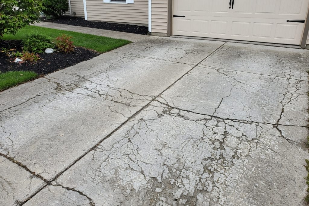 Scaled, cracked driveway slab beside a garage — Concrete Replacement in South Haven