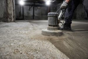 Worker grinding dust off a rough basement slab — Epoxy Flooring in Valparaiso