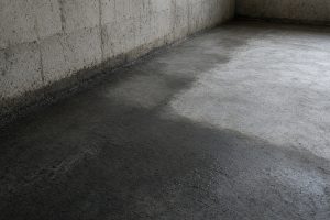 Dark damp band on an older basement slab beside the wall — Concrete Basements in Hebron