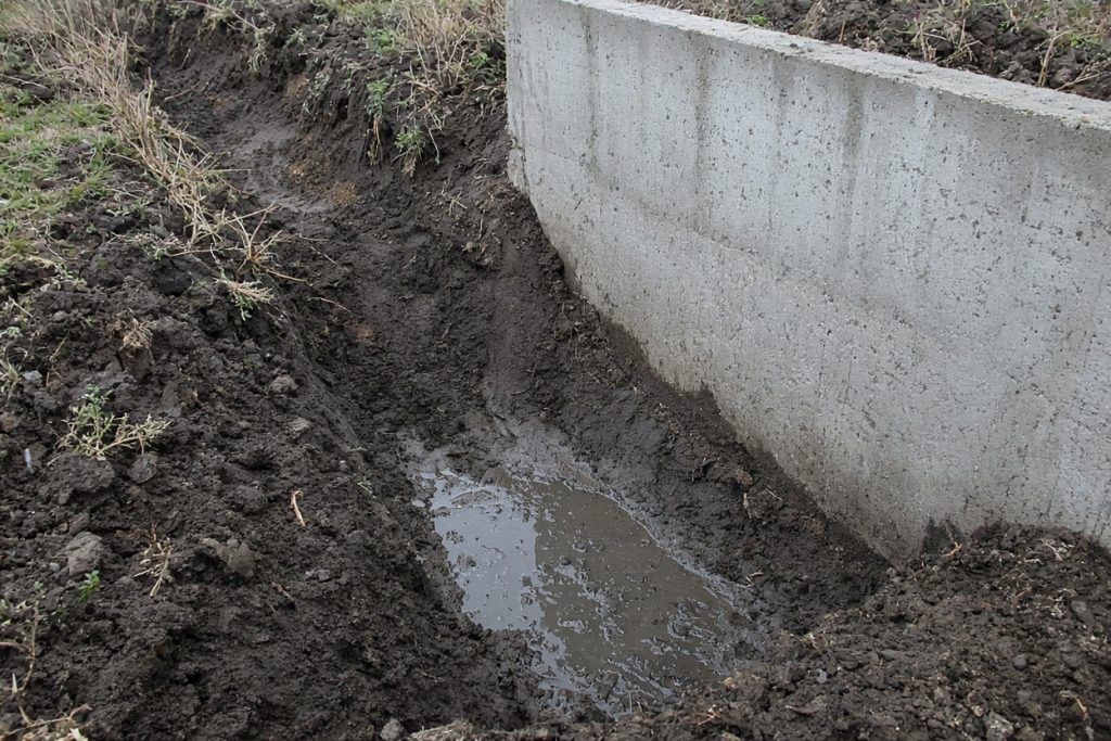 Standing water in a footing trench beside a house wall - Concrete Foundations in Hebron
