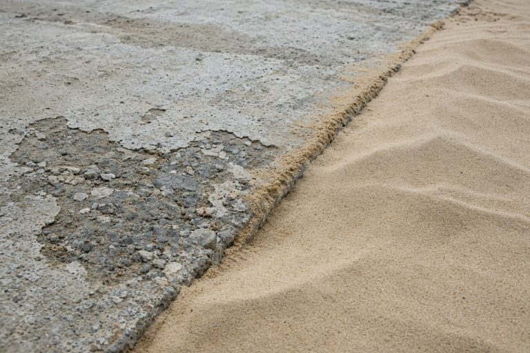 Sand drifted against a worn patio edge near the lake — Concrete Patios in Ogden Dunes