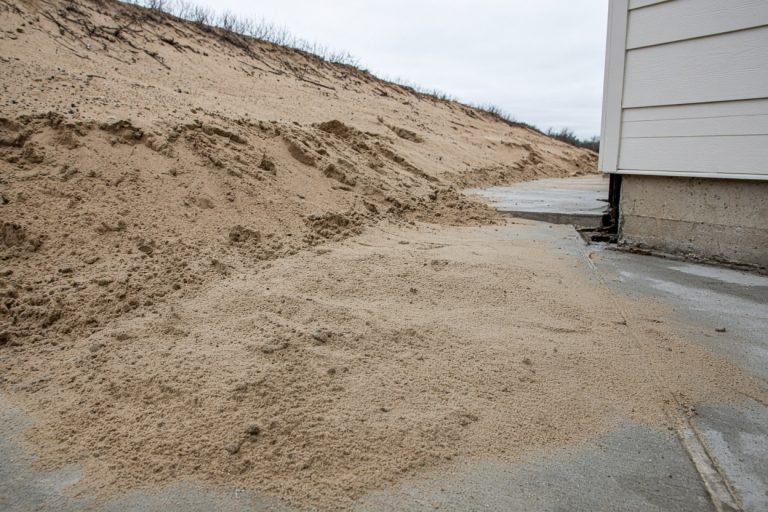 Sand washed over a side walk below a bare slope — Retaining Walls in Portage