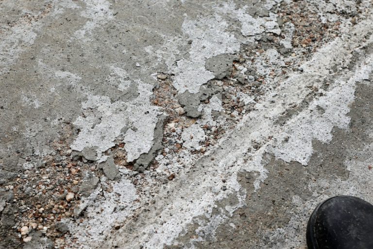 Flaking driveway surface with pale salt crust and exposed stone — Concrete Driveways in Porter